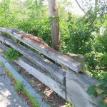 View of timber bridge railing showing a disconnected top rail that has lifted from its support, exposing fasteners and compromising safety.