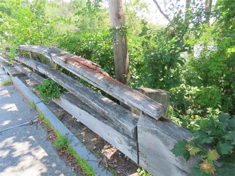 View of timber bridge railing showing a disconnected top rail that has lifted from its support, exposing fasteners and compromising safety.