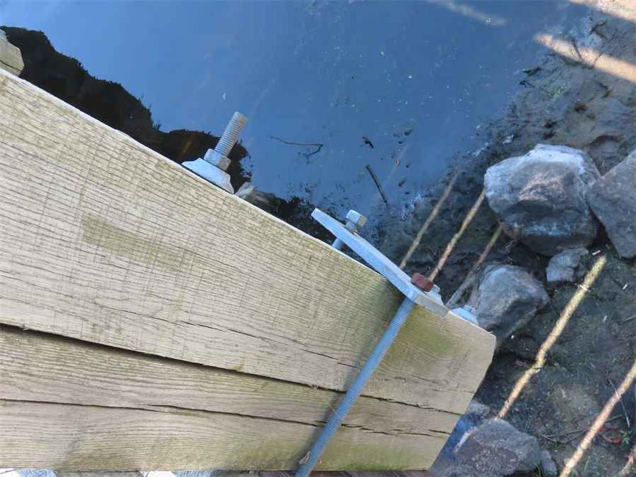 Close-up of the north bridge railing showing a metal bolt protruding and a loose bracket at the east end, with visible misalignment.
