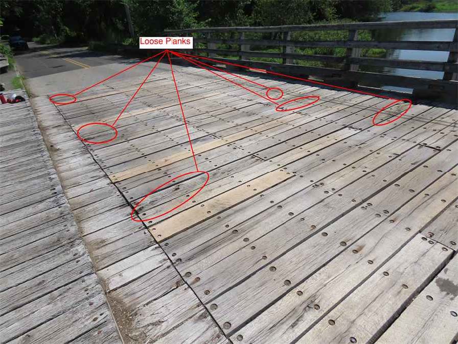 Midspan view of timber bridge deck looking east, showing weathered planks with signs of wear, discoloration, and minor splitting along the surface. Six portions are circled and labelled as loose planks.