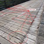 View of the timber bridge deck midspan looking west, revealing worn and uneven planks with scattered darkened areas suggesting moisture exposure. Eight portions are circled and labelled as loose planks.